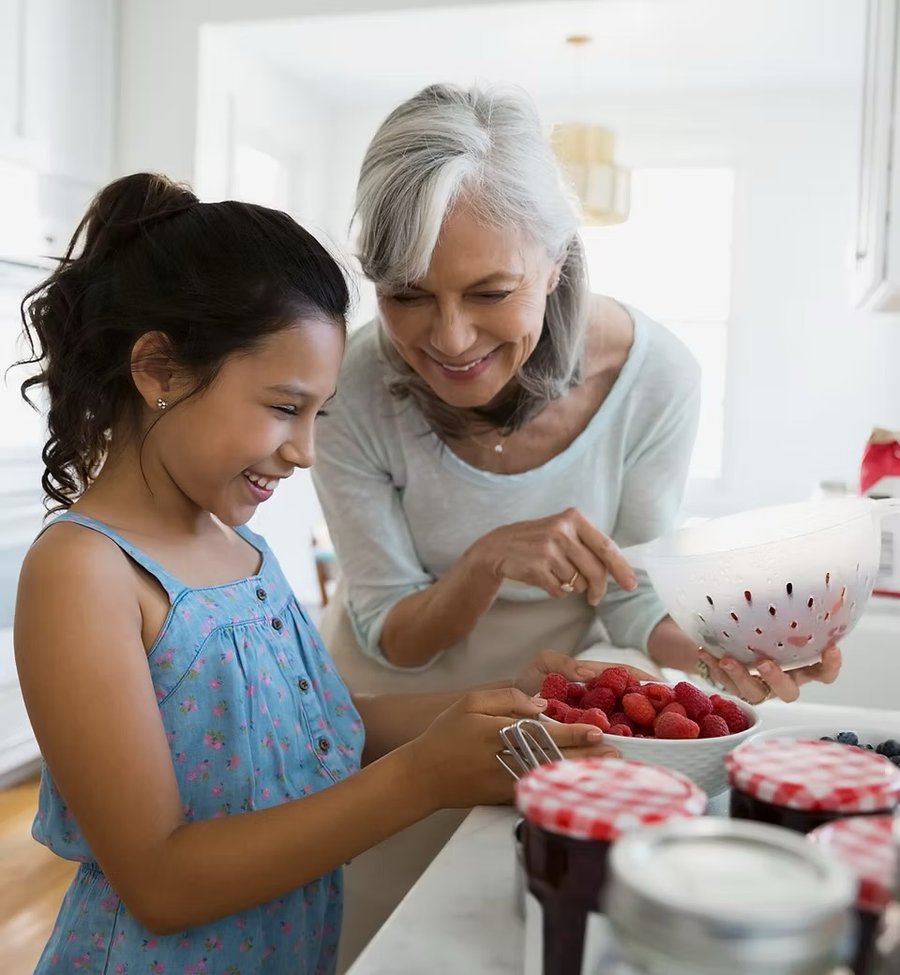 A grandmother and her granddaughter preparing fruit together in the kitchen