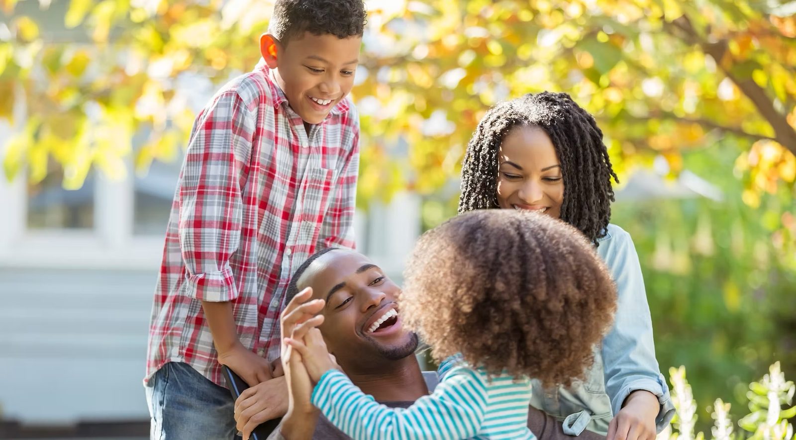 Parents and their two children laughing together in the front yard of their home